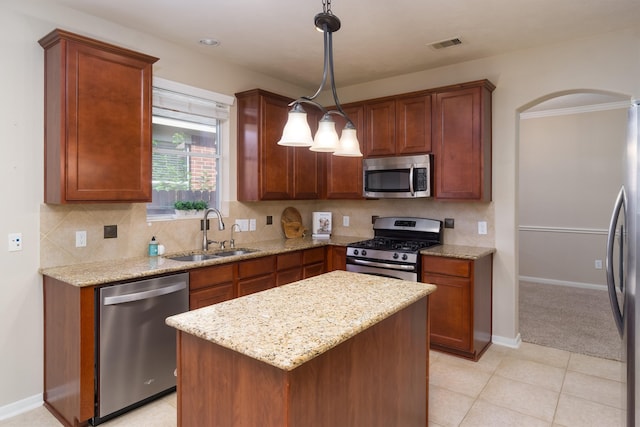 kitchen with light stone counters, stainless steel appliances, sink, decorative light fixtures, and a kitchen island