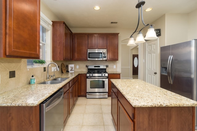 kitchen with light stone countertops, appliances with stainless steel finishes, tasteful backsplash, sink, and pendant lighting