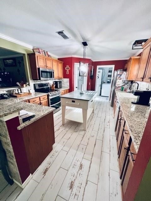 kitchen featuring appliances with stainless steel finishes, decorative light fixtures, light stone counters, and light hardwood / wood-style floors