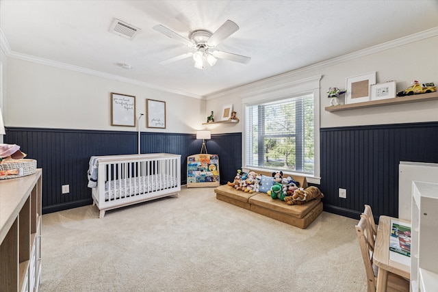 carpeted bedroom featuring ceiling fan, crown molding, and a crib