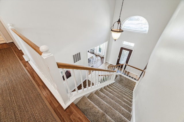 stairway with wood-type flooring and a towering ceiling