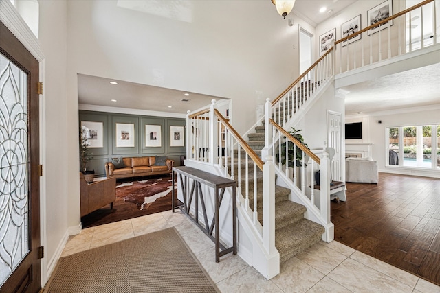 foyer entrance featuring crown molding, light hardwood / wood-style flooring, and a towering ceiling