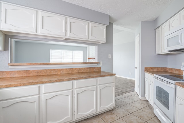 kitchen with a textured ceiling, white cabinetry, light tile patterned floors, and white appliances