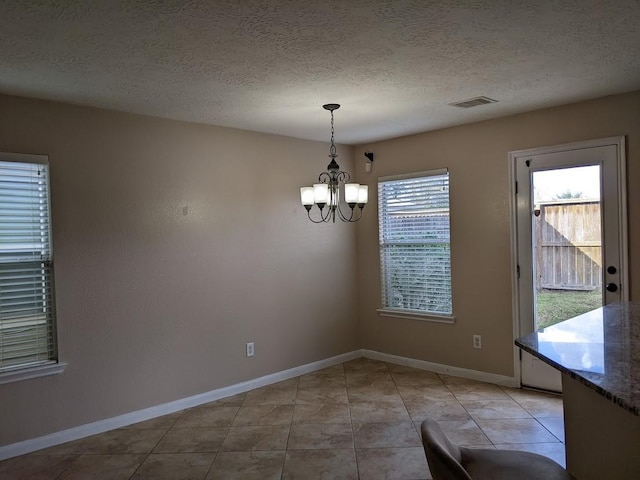 unfurnished dining area with a wealth of natural light, a textured ceiling, and an inviting chandelier