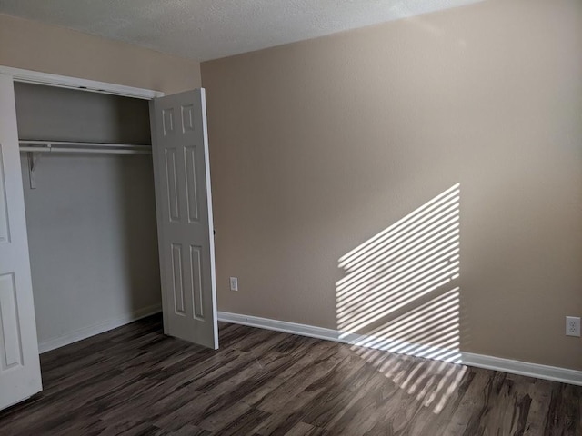 unfurnished bedroom featuring a textured ceiling, dark wood-type flooring, and a closet