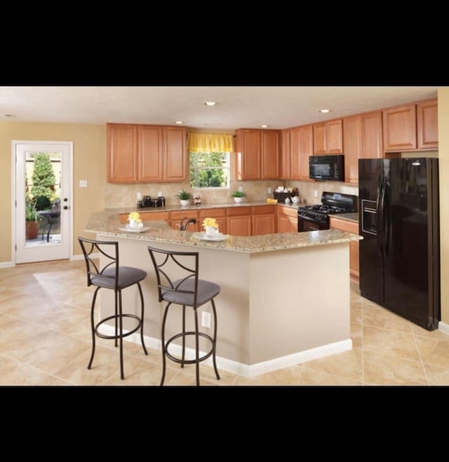 kitchen with a breakfast bar, light tile patterned flooring, light stone counters, and black appliances