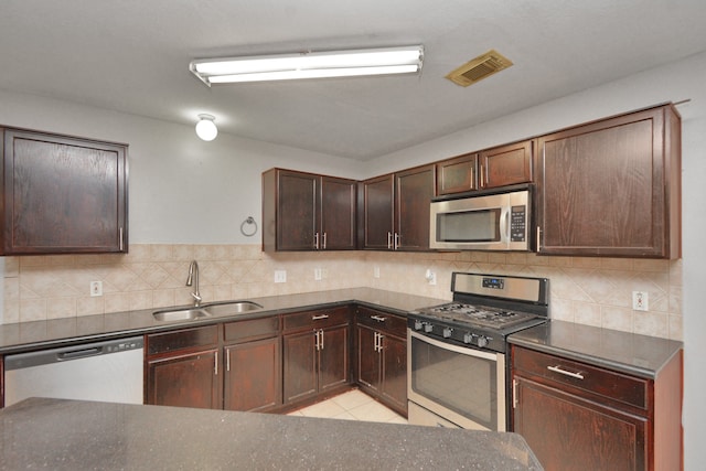 kitchen with appliances with stainless steel finishes, tasteful backsplash, dark brown cabinets, sink, and light tile patterned floors