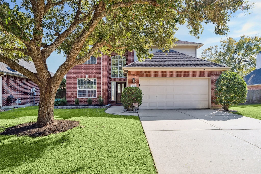 traditional-style house featuring an attached garage, brick siding, a shingled roof, concrete driveway, and a front yard