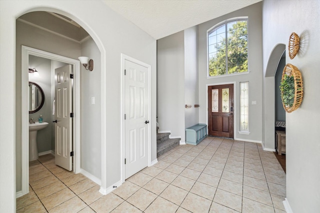 foyer featuring light tile patterned floors, a textured ceiling, arched walkways, a towering ceiling, and baseboards