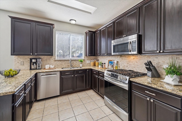 kitchen with light tile patterned floors, stainless steel appliances, tasteful backsplash, a sink, and light stone countertops