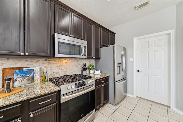 kitchen featuring light tile patterned floors, stainless steel appliances, visible vents, dark brown cabinetry, and light stone countertops