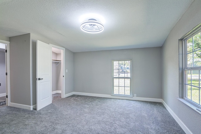 unfurnished bedroom with carpet, a closet, a spacious closet, and a textured ceiling