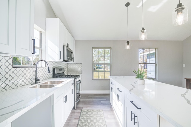 kitchen with appliances with stainless steel finishes, white cabinetry, sink, hanging light fixtures, and light stone counters