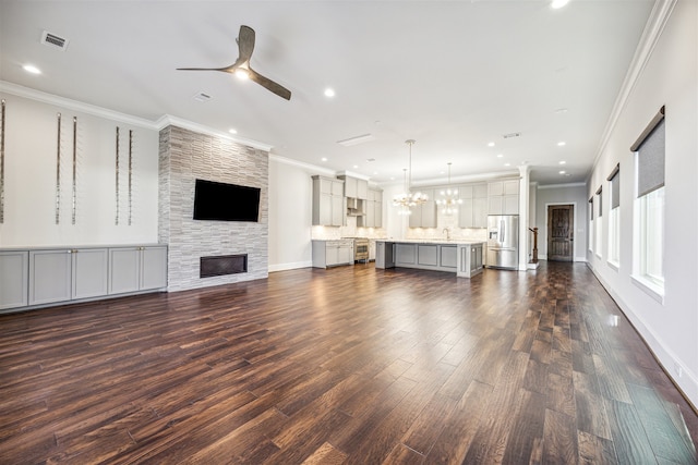 unfurnished living room featuring a fireplace, ceiling fan with notable chandelier, dark wood-type flooring, and ornamental molding