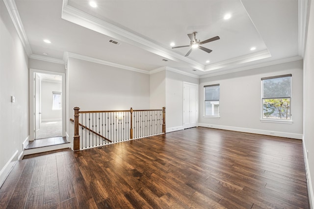 empty room with a tray ceiling, crown molding, dark hardwood / wood-style flooring, and ceiling fan