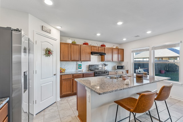 kitchen featuring sink, a kitchen breakfast bar, decorative backsplash, a center island with sink, and appliances with stainless steel finishes