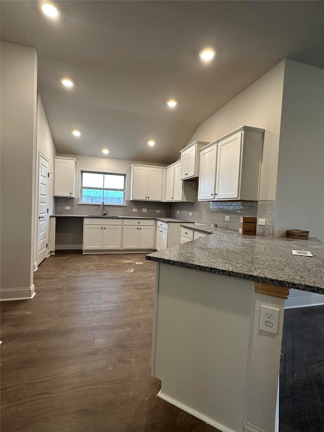 kitchen with kitchen peninsula, dark stone counters, dark wood-type flooring, sink, and white cabinetry