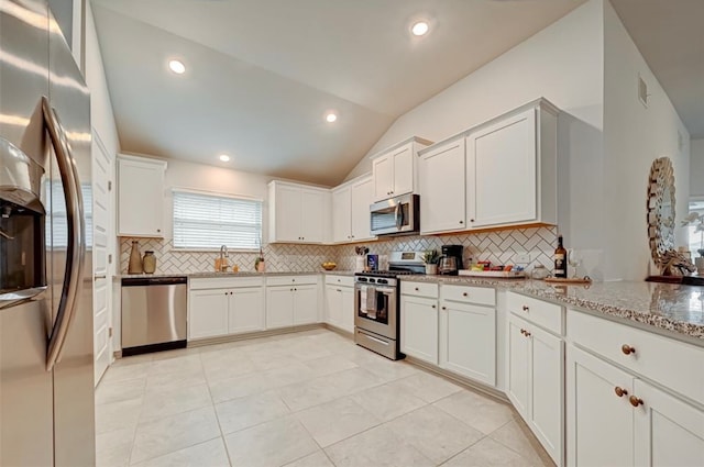 kitchen with white cabinets, light stone countertops, appliances with stainless steel finishes, and vaulted ceiling