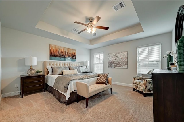 carpeted bedroom with a raised ceiling, multiple windows, and ceiling fan