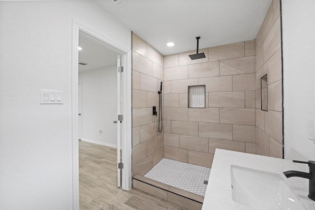 bathroom with a tile shower, vanity, and wood-type flooring