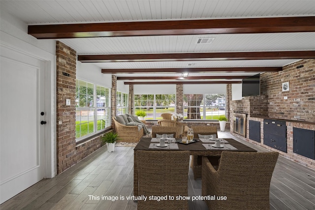 dining area featuring hardwood / wood-style flooring, plenty of natural light, beamed ceiling, and brick wall