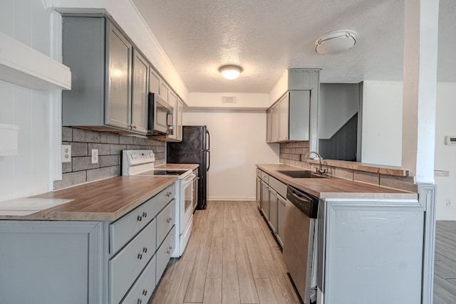 kitchen featuring sink, light hardwood / wood-style flooring, gray cabinets, appliances with stainless steel finishes, and tasteful backsplash