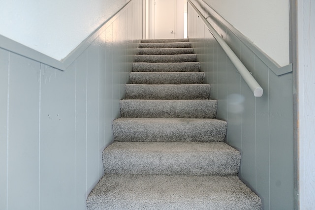 stairway featuring wood walls and carpet floors