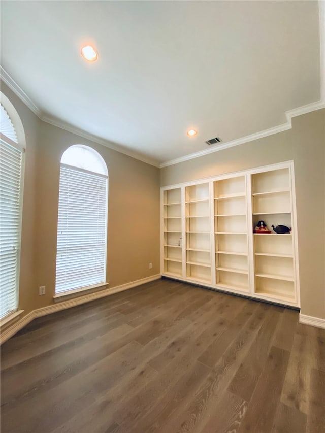 spare room with crown molding, built in features, and dark hardwood / wood-style flooring