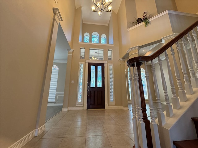 tiled foyer featuring a high ceiling, ornamental molding, a chandelier, and ornate columns