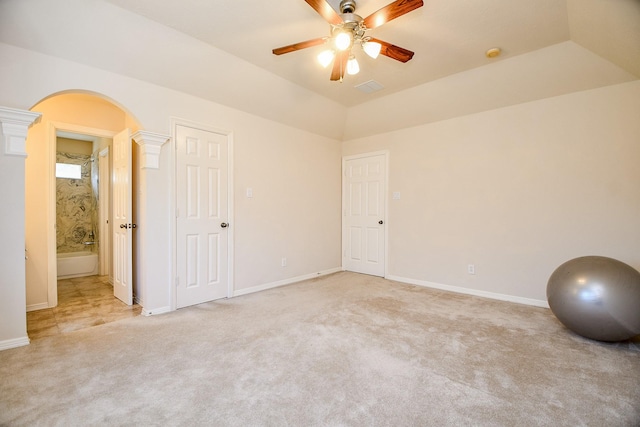 interior space with ensuite bath, ceiling fan, decorative columns, light colored carpet, and vaulted ceiling