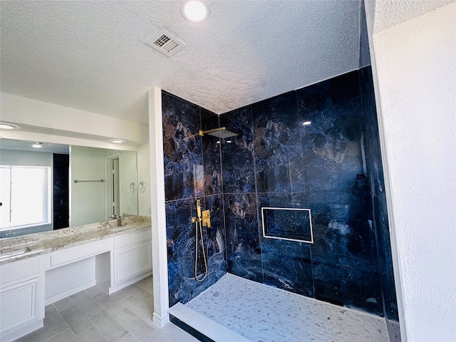 bathroom with a textured ceiling, vanity, and tiled shower