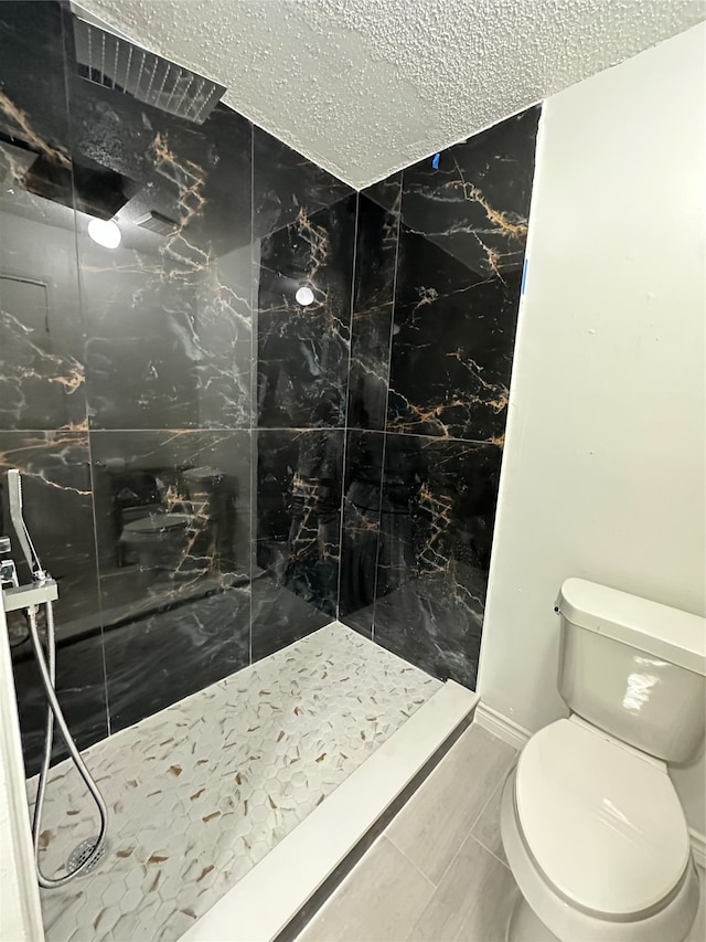 bathroom with a tile shower, a textured ceiling, and toilet