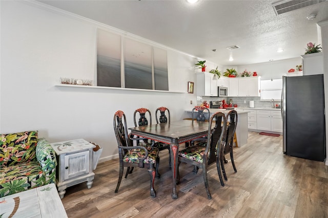 dining space featuring light hardwood / wood-style flooring, a textured ceiling, and ornamental molding