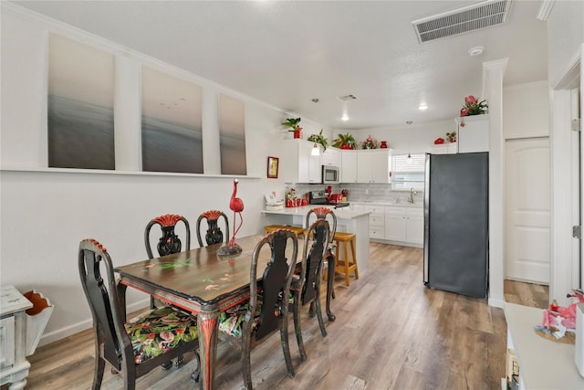 dining area with sink, light wood-type flooring, and crown molding