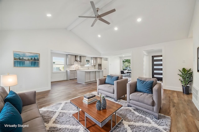 living room with ceiling fan, sink, beam ceiling, high vaulted ceiling, and light hardwood / wood-style floors