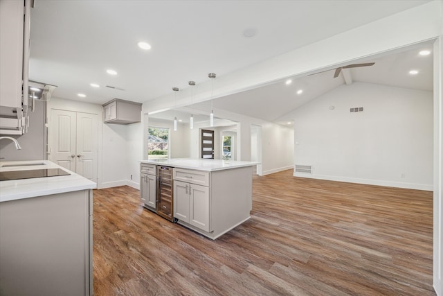 kitchen featuring pendant lighting, ceiling fan, vaulted ceiling with beams, wood-type flooring, and beverage cooler