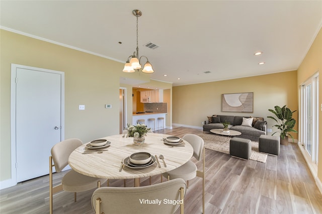 dining space with ornamental molding, a chandelier, and light hardwood / wood-style floors