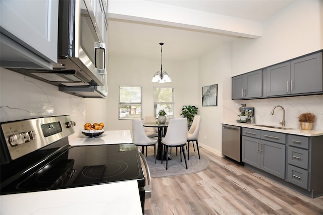 kitchen featuring sink, stainless steel appliances, an inviting chandelier, light hardwood / wood-style flooring, and pendant lighting