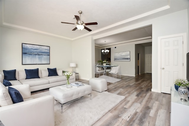 living room featuring ceiling fan with notable chandelier, a raised ceiling, wood-type flooring, and ornamental molding