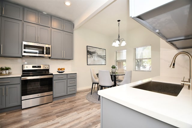 kitchen featuring light wood-type flooring, stainless steel appliances, sink, gray cabinets, and hanging light fixtures