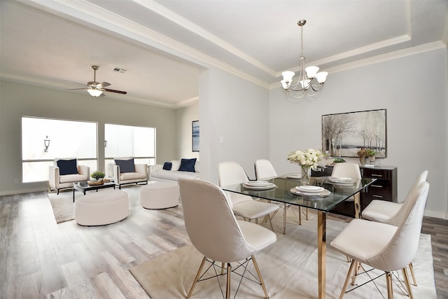 dining area with ceiling fan with notable chandelier, light wood-type flooring, crown molding, and a tray ceiling