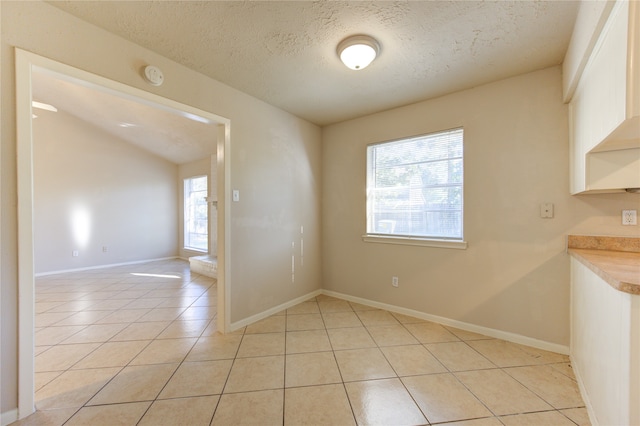 unfurnished dining area featuring vaulted ceiling, light tile patterned floors, a healthy amount of sunlight, and a textured ceiling