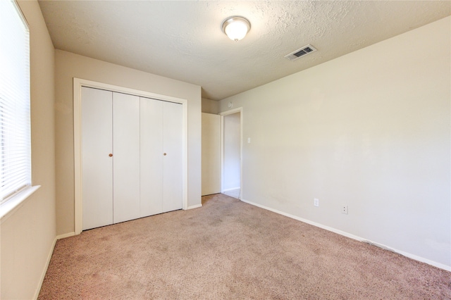 unfurnished bedroom with a closet, light colored carpet, and a textured ceiling