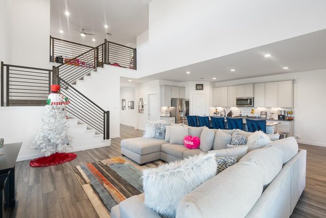 living room with ceiling fan, a towering ceiling, and hardwood / wood-style floors