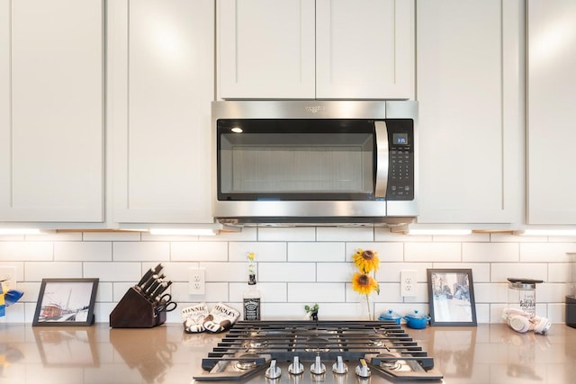 interior details with appliances with stainless steel finishes, backsplash, and white cabinets