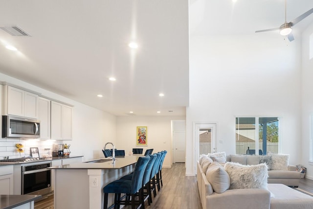 kitchen with a breakfast bar area, appliances with stainless steel finishes, backsplash, a kitchen island with sink, and sink