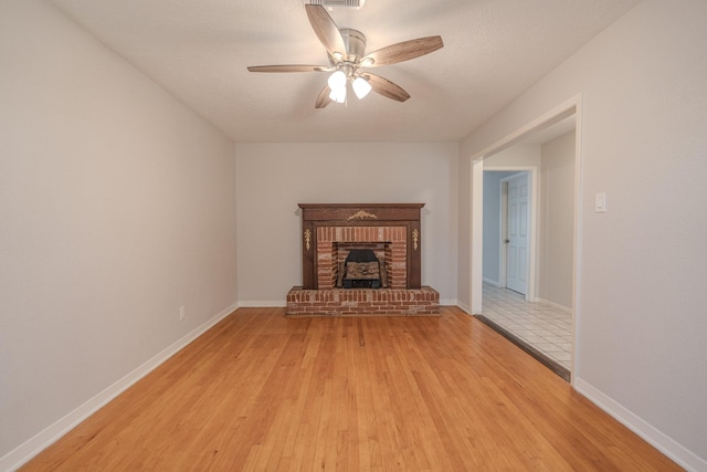 unfurnished living room featuring a brick fireplace, ceiling fan, a textured ceiling, and light hardwood / wood-style flooring