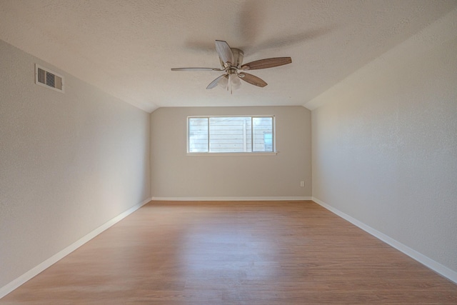 empty room featuring ceiling fan, lofted ceiling, a textured ceiling, and light hardwood / wood-style flooring