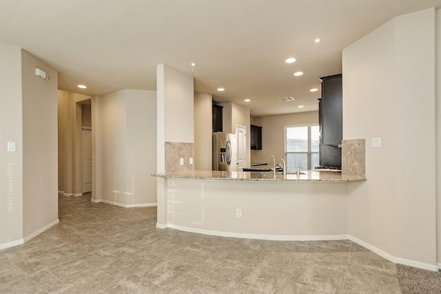 kitchen with light stone countertops, stainless steel fridge with ice dispenser, kitchen peninsula, and tasteful backsplash