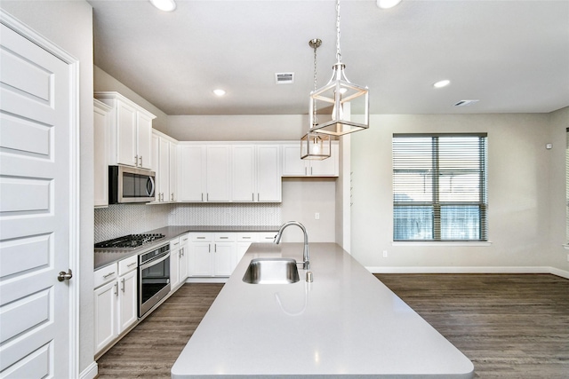 kitchen with appliances with stainless steel finishes, decorative light fixtures, white cabinetry, sink, and a center island with sink